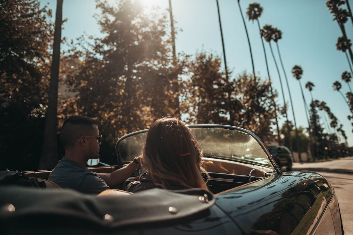 Man and Lady in convertible car driving towards the sun