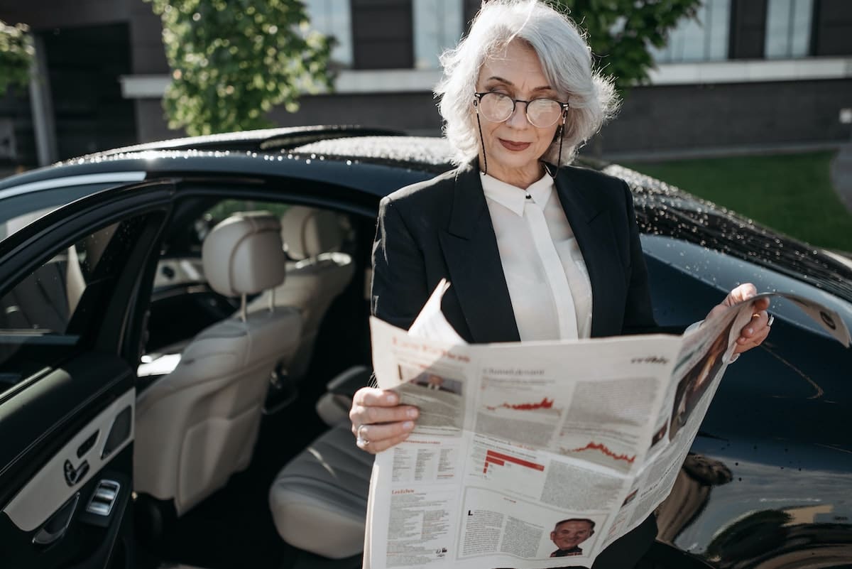 Business Lady reading newspaper outside her car