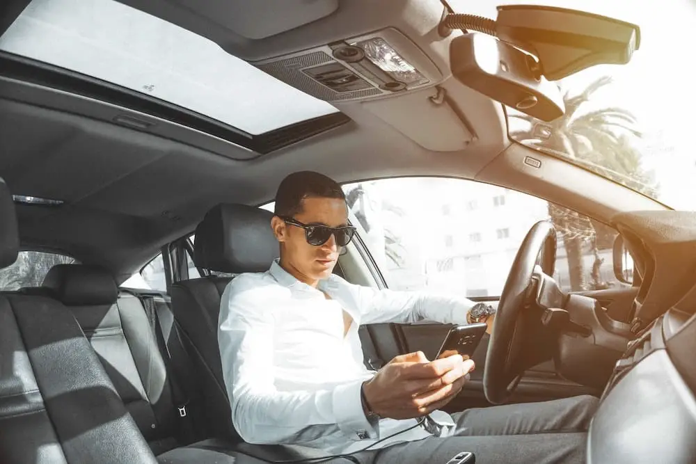 Man sat in his car lookin gat the best car subscription deals on his smartphone
