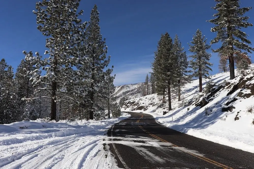 Snow covered Road in the hills with trees.